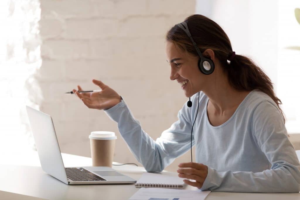Side view head shot smiling mixed race lady freelancer wearing headset, communicating with client via video computer call