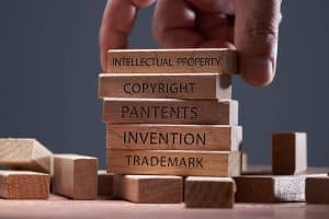 man adding a block showing the words Intellectual property on top of other wooden block with text copyright, patents, invention, and trademark