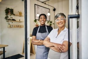 Coffee shop, senior woman manager portrait with barista feeling happy about shop success.